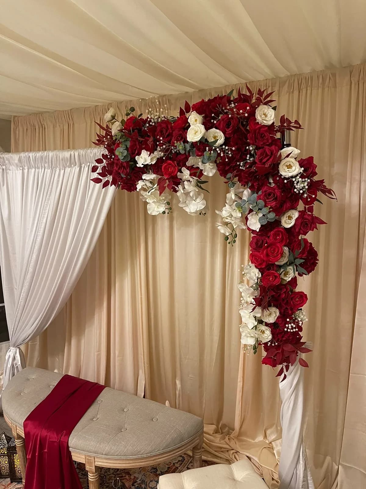 Close view of the red rose, white rose and orchid floral arch from a baraat stage, over ivory drapes beneath a draped ceiling