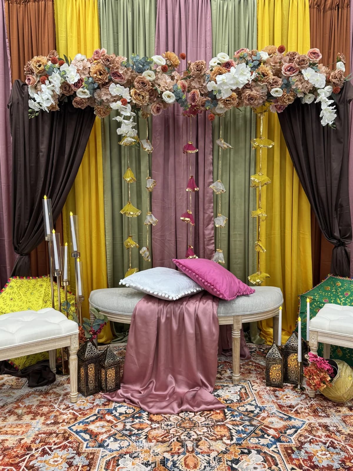 Mehndi stage with sage, mustard, dusky pink and chocolate drapes, a blush rose garland, gota flower hangings, candles and embroidered parasols